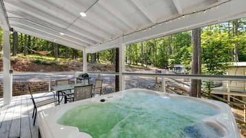 A hot tub under a covered deck with a view of a forested area.