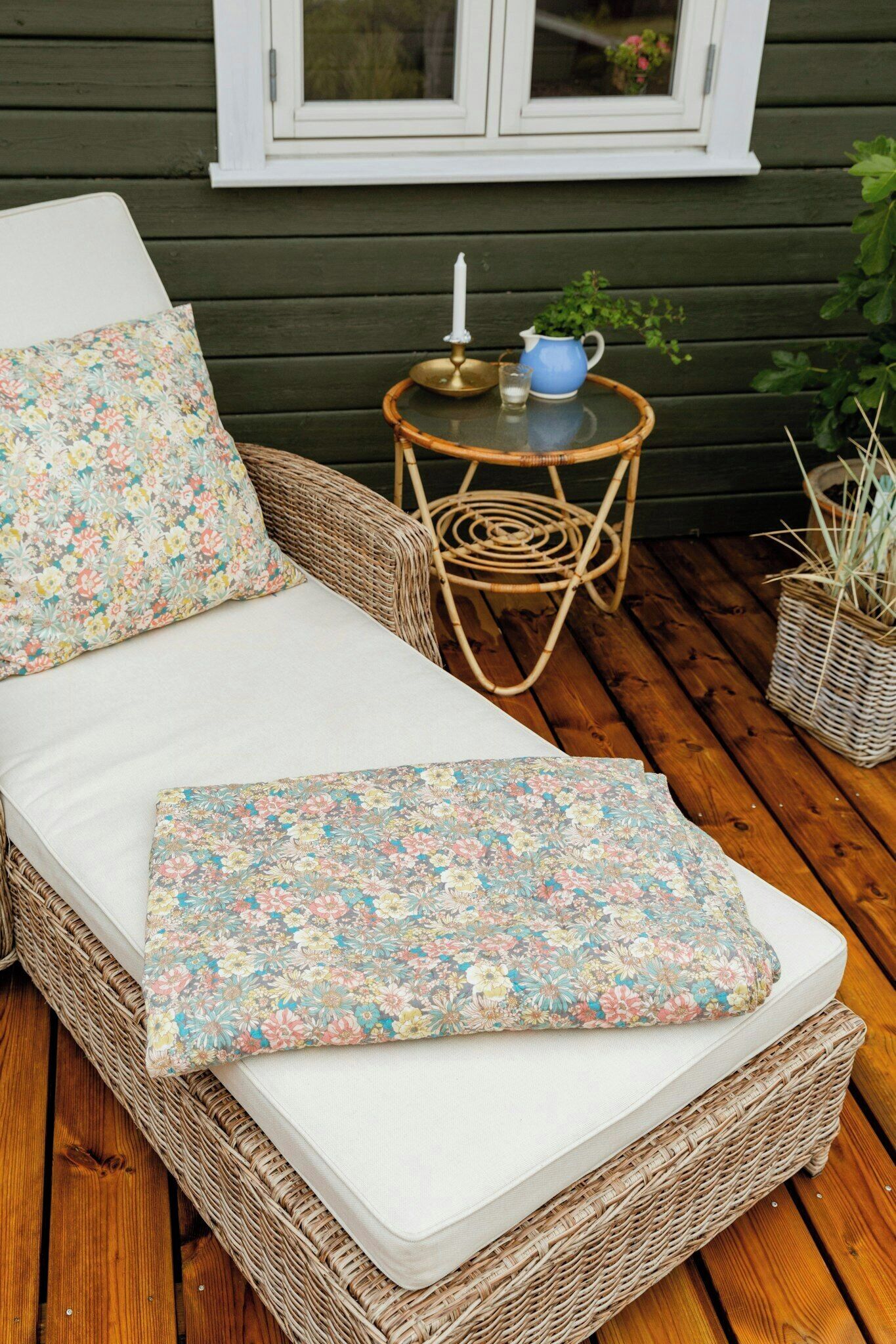 En fletsofa med pude og tæppe i blomstermønster, placeret på en træterrasse.