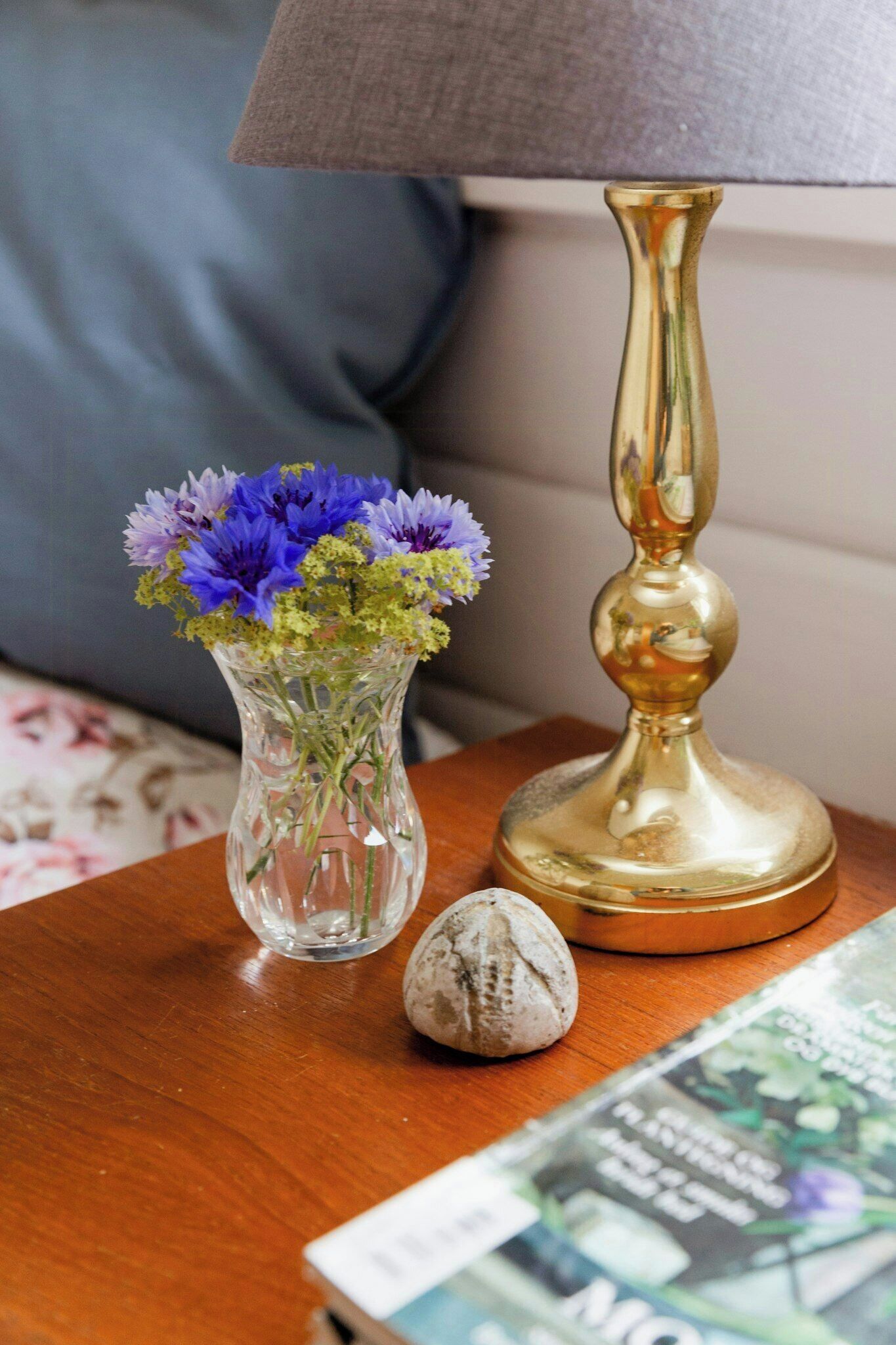 Een glazen vaas met bloemen, een lamp en een boek op een houten tafel.
