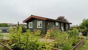 Una casa con facciata verde, rivestimenti bianchi e tetto rosso, circondata da aiuole rialzate con diverse piante.