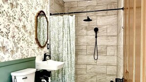 A bathroom with a toilet, sink, shower, and a mirror.