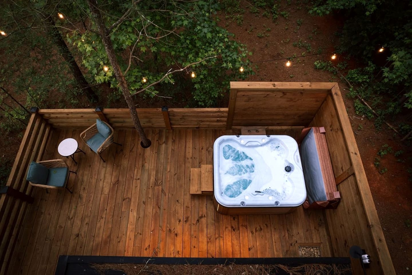 Une terrasse en bois avec un jacuzzi, un espace salon et des guirlandes lumineuses.