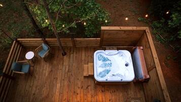Une terrasse en bois avec un jacuzzi, un espace salon et des guirlandes lumineuses.