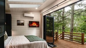 Un dormitorio con cama, televisión, chimenea y balcón con vistas a árboles.