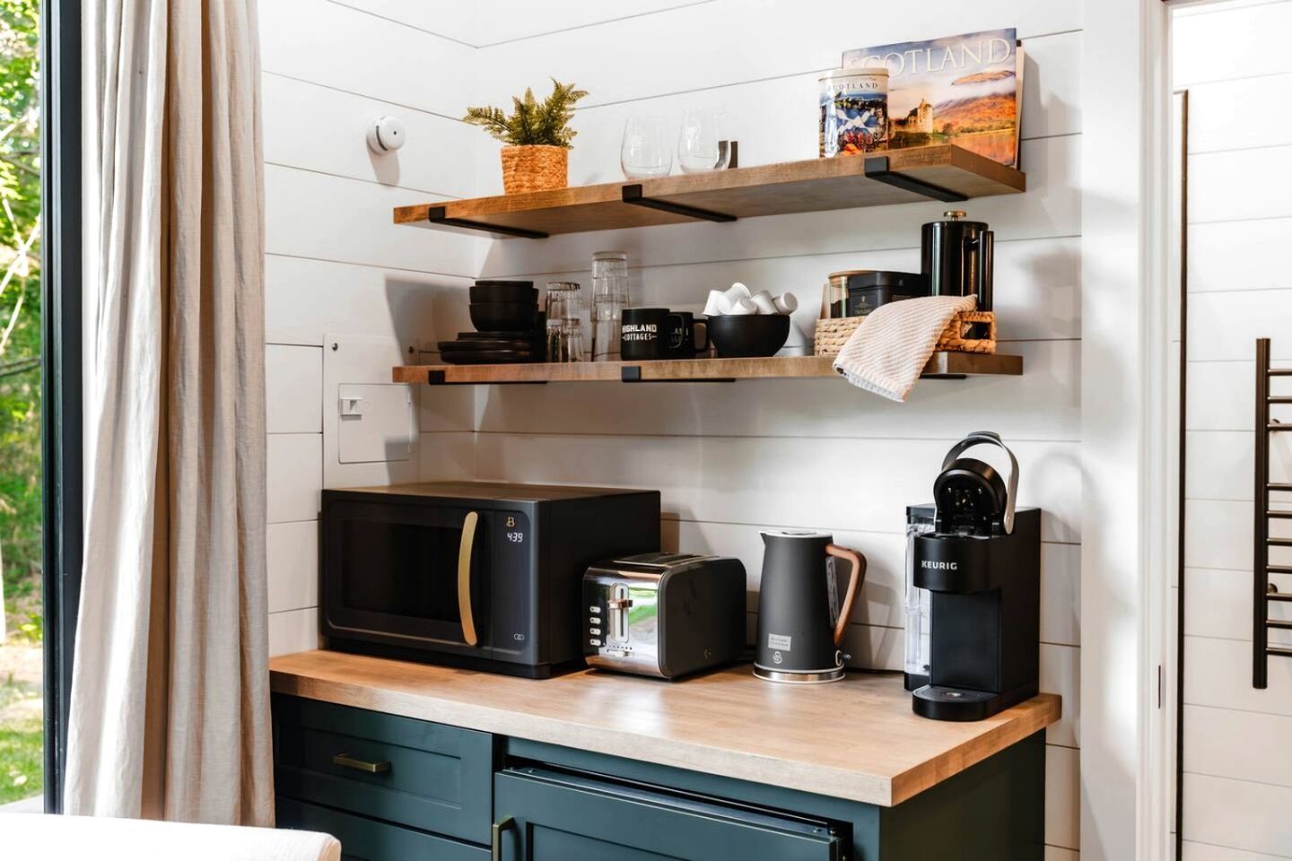 Une cuisine compacte équipée d’un four à micro-ondes, d’un grille-pain, d’une machine à café et d’étagères contenant des ustensiles de cuisine.