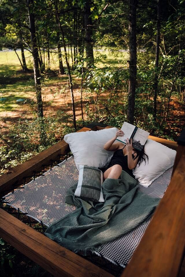 A hammock in a forested area with a person reading a book.