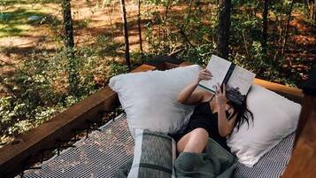A hammock in a forested area with a person reading a book.