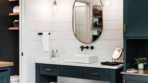 Un baño moderno con un tocador blanco, muebles oscuros, un espejo grande e iluminación colgante.
