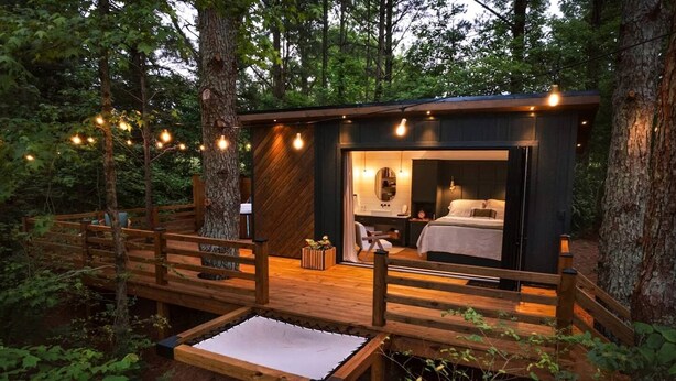 Una cabaña tipo casa del árbol con una terraza de madera, una cama y un baño.