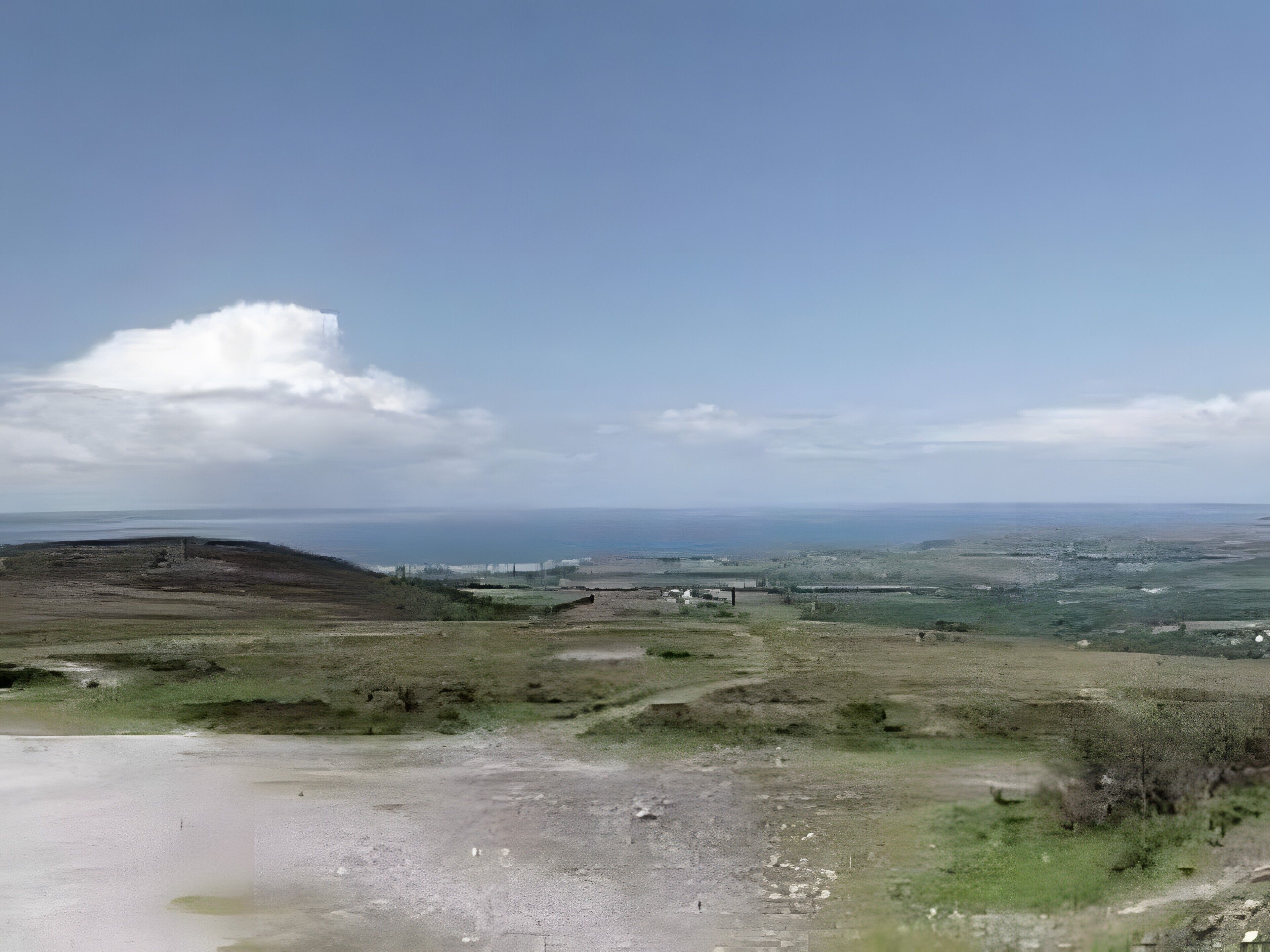 A coastal landscape with a clear sky, distant horizon, and sparse vegetation.