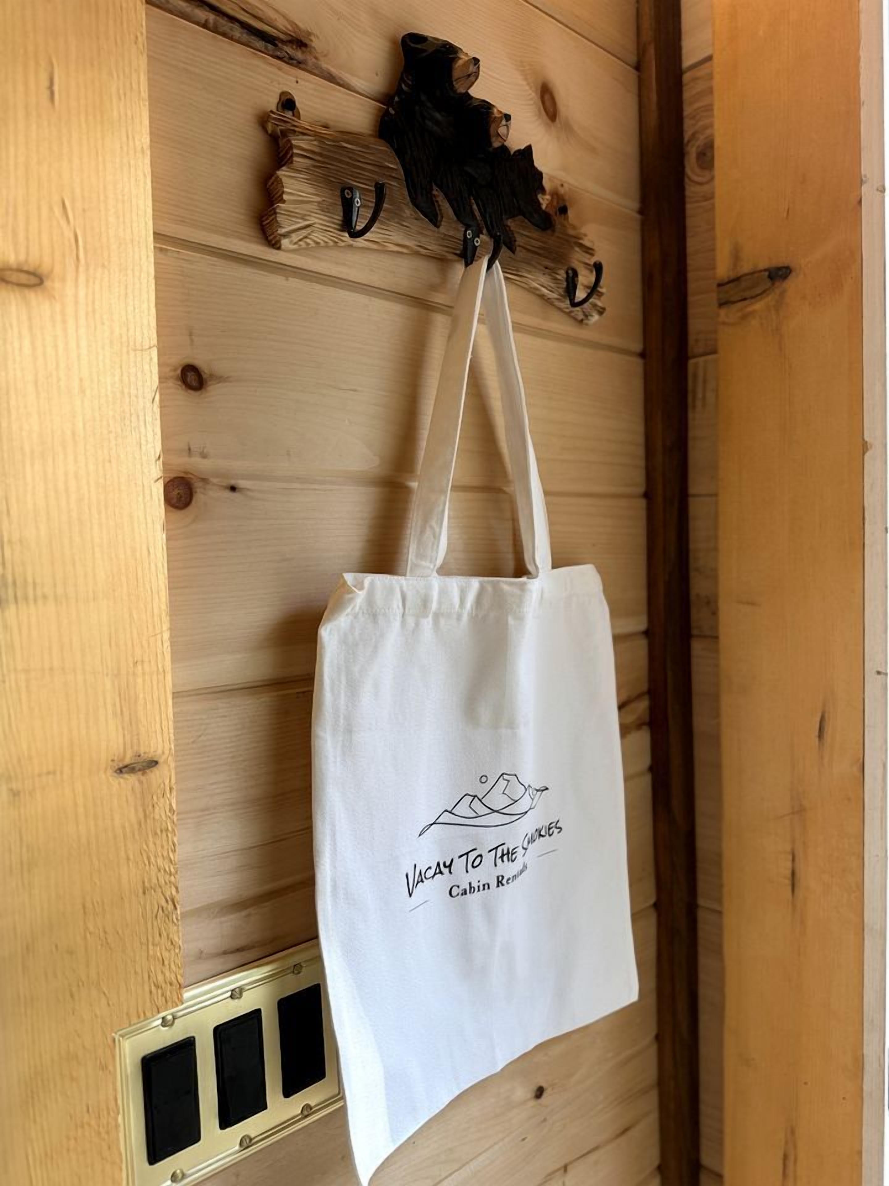 Una bolsa de tela blanca colgada en una pared de madera con diseño rústico, un gancho metálico y una rejilla debajo.