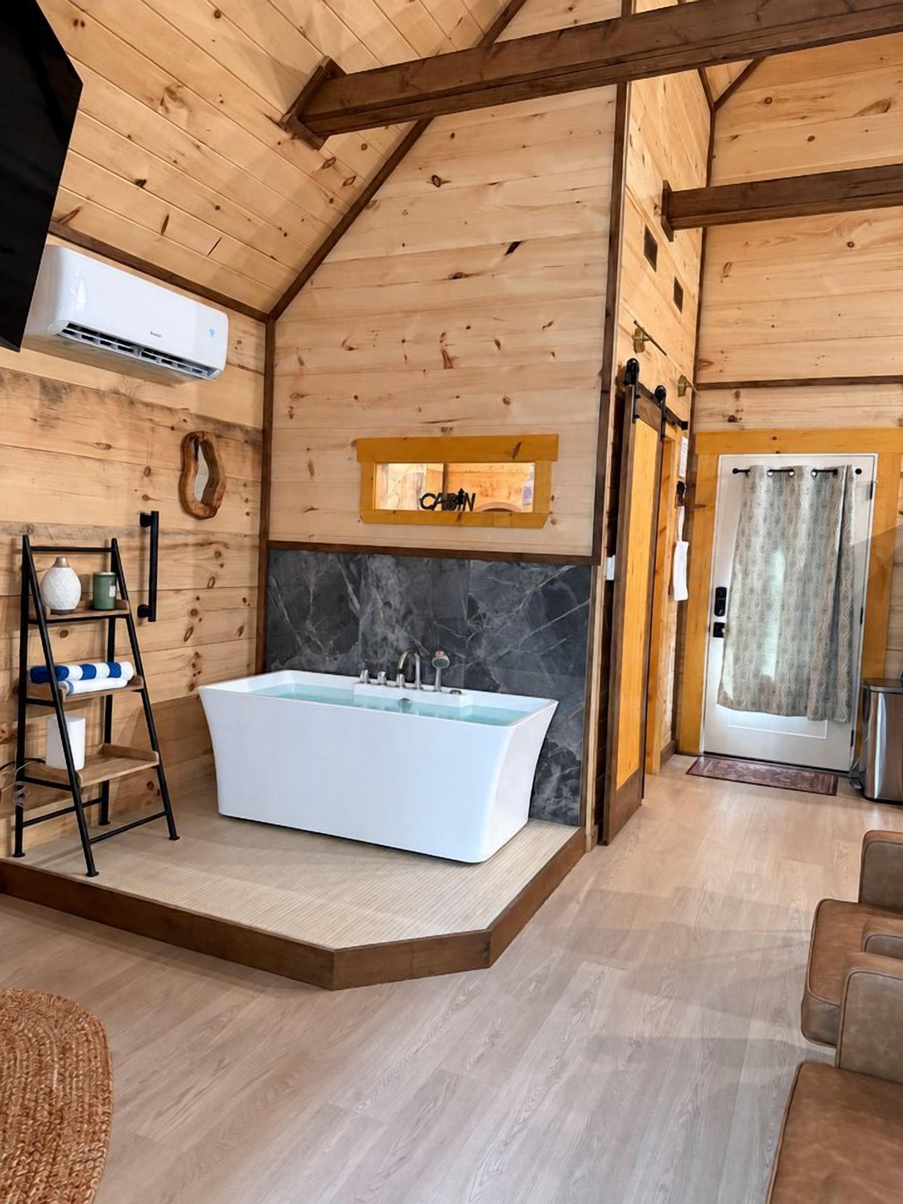A modern bathroom with a freestanding bathtub, wooden walls, and a marble accent wall.