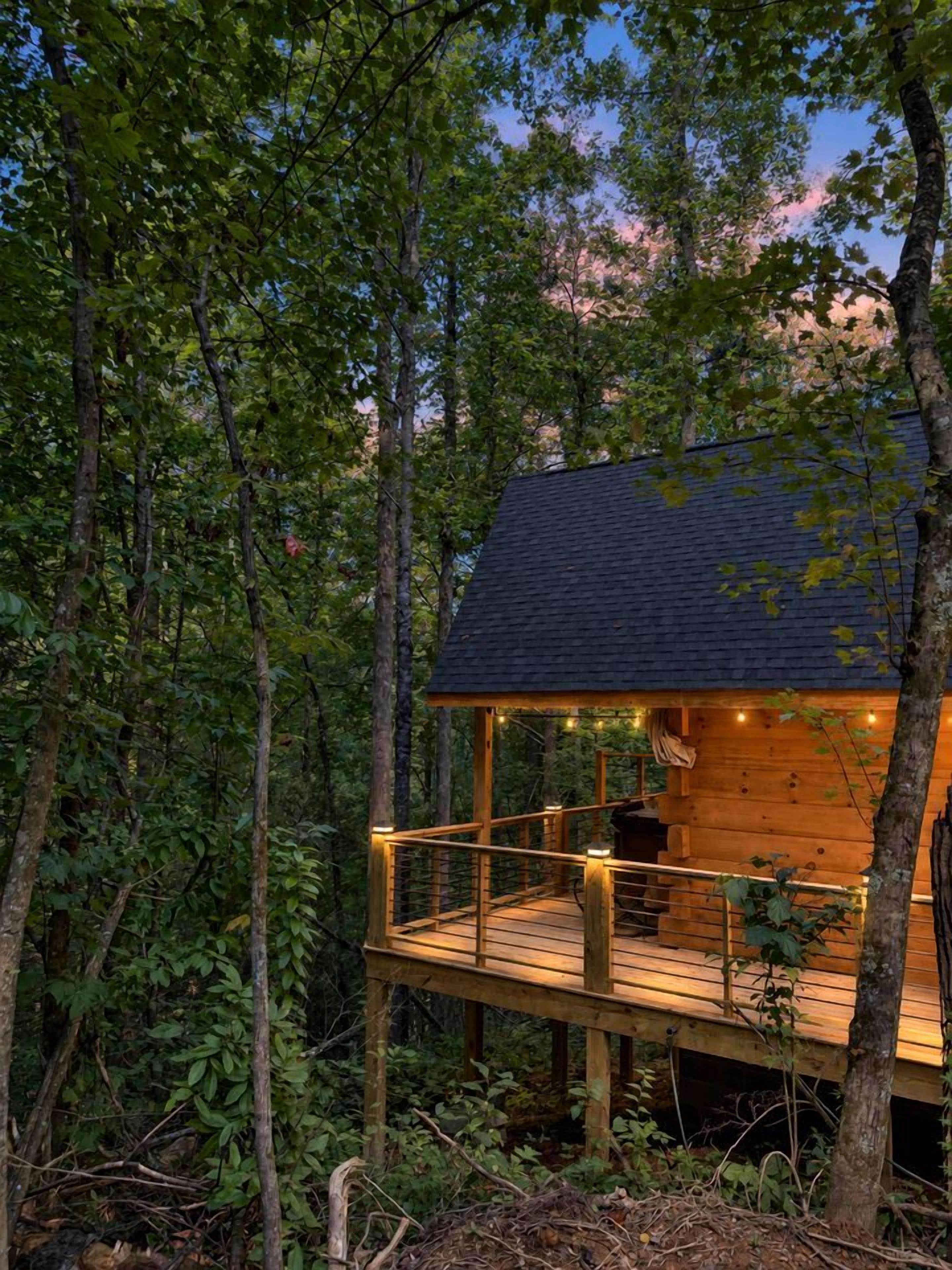 A wooden cabin with a deck, surrounded by trees.