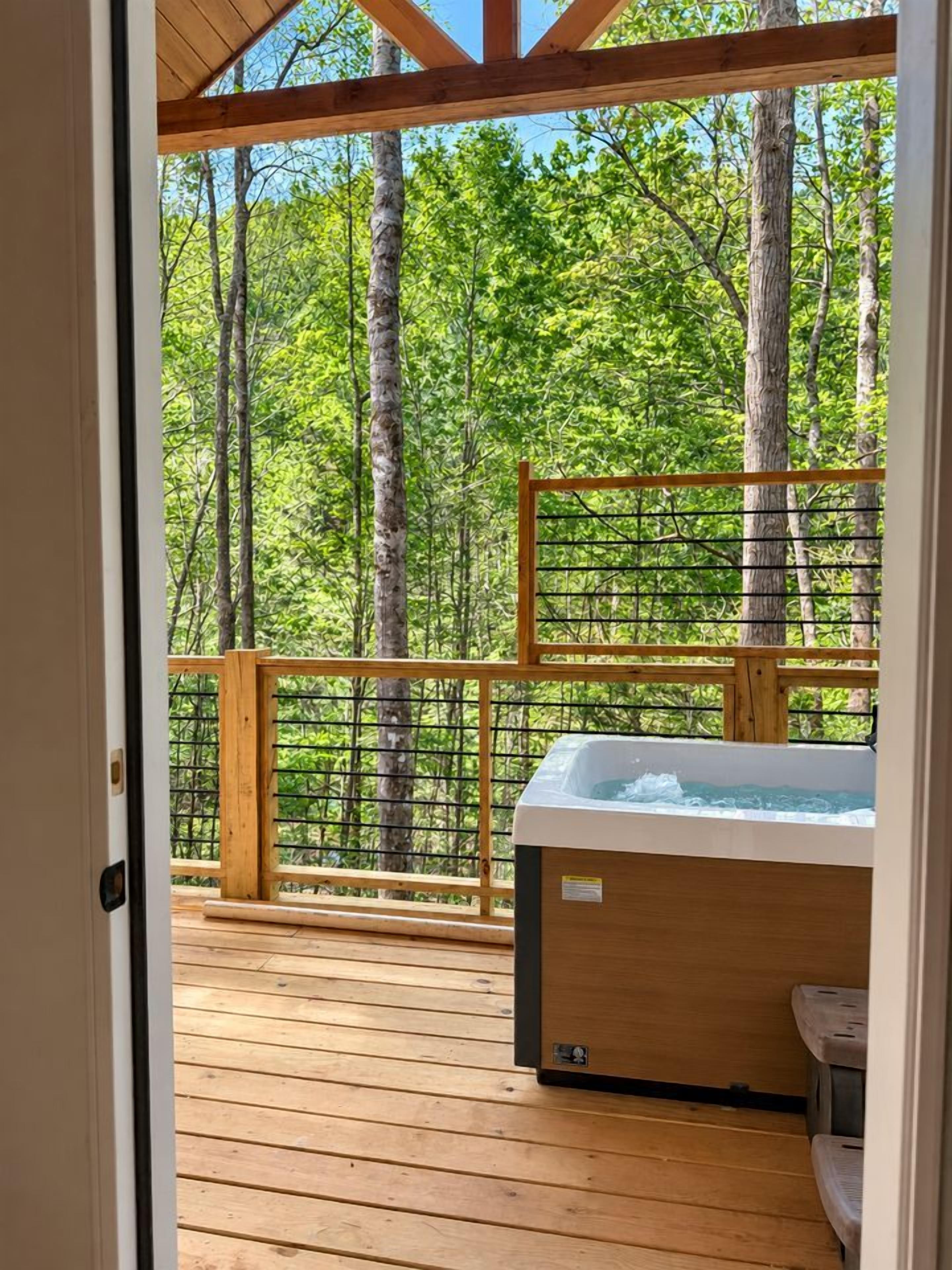 Eine Holzterrasse mit Whirlpool, umgeben von einem Holgitter und Blick auf einen Wald.