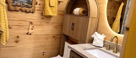 A bathroom with wooden walls, a white toilet, a sink with a gold faucet, and a towel rack with yellow towels.