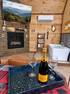 A cozy room with a fireplace, a large TV, a bathtub, and a bottle of champagne on a tray. - Luxury Romantic Cabin With Hot Tub in Gatlinburg Tennessee Golden Forest Smoky Mountains (Sevierville)