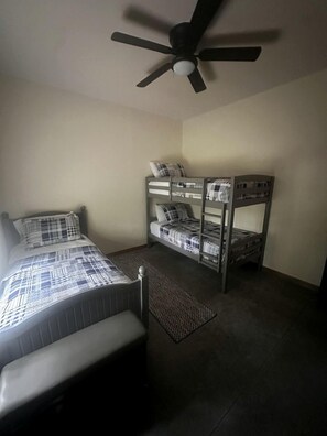 Une chambre avec un lit, un lit superposé, un ventilateur de plafond et un tapis.