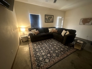 A living room with a sectional sofa, a patterned rug, a side table with a lamp, and a framed picture on the wall.