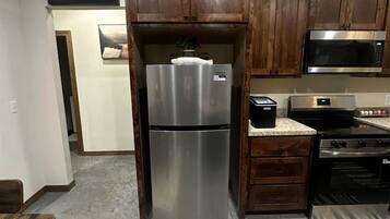 A kitchen with wooden cabinets, a stainless steel refrigerator, a microwave, and a stove.