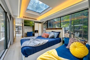 Ein modernes Schlafzimmer mit Dachfenster, einem Bett, einer Couch und Blick ins Freie.