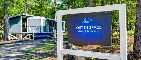 Señal con el texto 'LOST IN SPACE' y 'STELLAR GATEWAYS', una cabaña y un área boscosa.