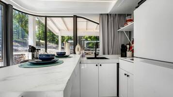 A modern kitchen with a large island, white cabinetry, and a view of a forested area.