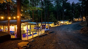 Ein rustikales Hotel im Chalet-Stil mit mehreren Zimmern, einer überdachten Sitzgelegenheit im Freien und einem Feldweg, der durch den Wald führt.