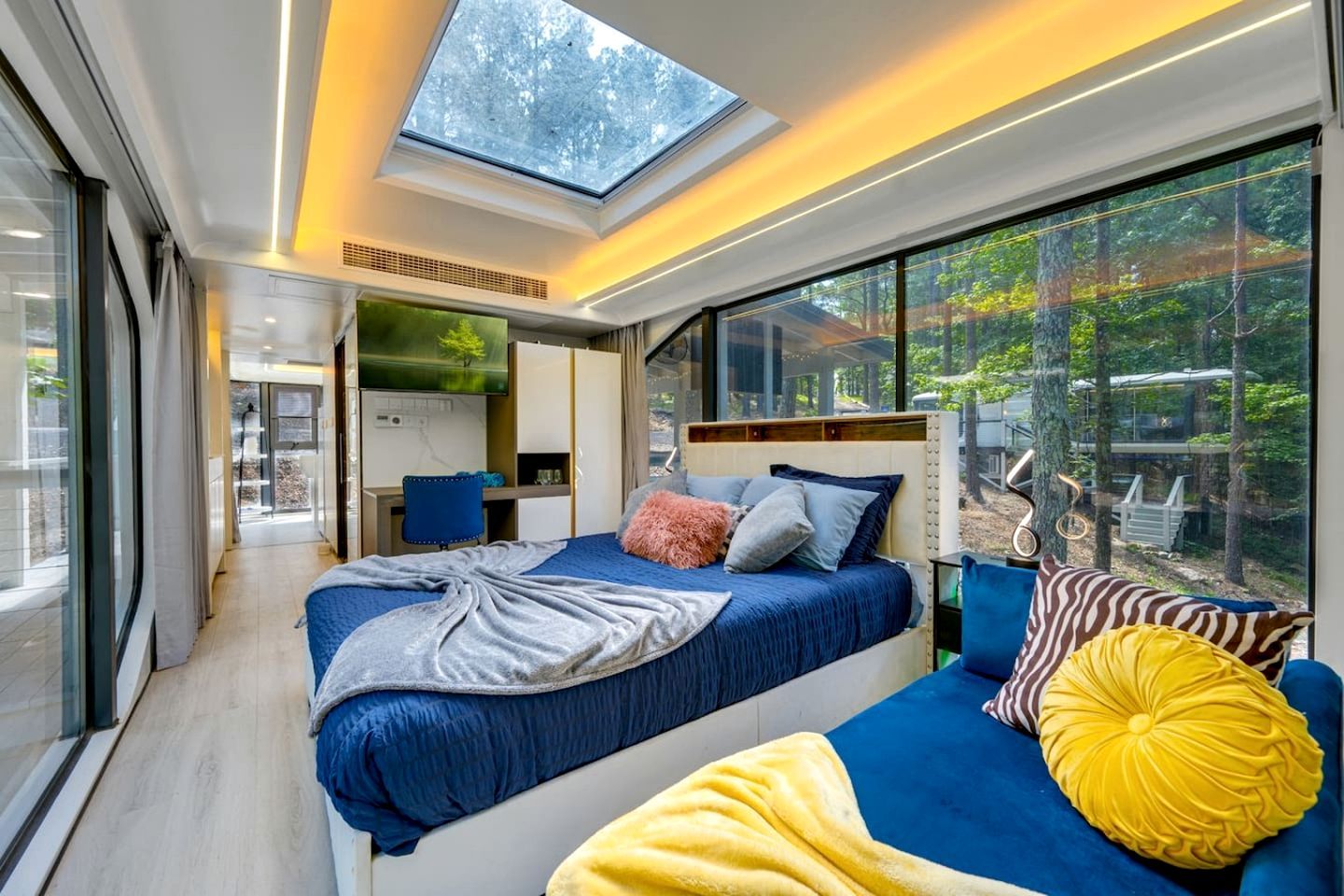 A modern bedroom with a skylight, a bed, a sofa, and a view of the outdoors.