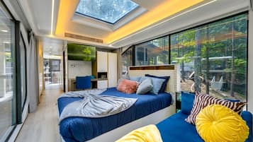 A modern bedroom with a skylight, a bed, a sofa, and a view of the outdoors.