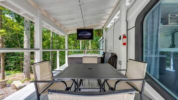 Un área de comedor al aire libre techada, con una mesa, sillas, una pantalla de televisión y un extintor.