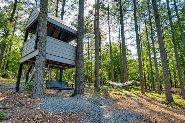 A treehouse with a bench and hammock in a forest.