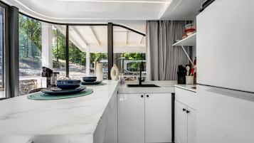 A modern kitchen with a large island, white cabinetry, and a view of a forested area.