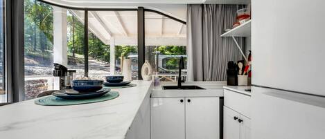 A modern kitchen with a large island, white cabinetry, and a view of a forested area.