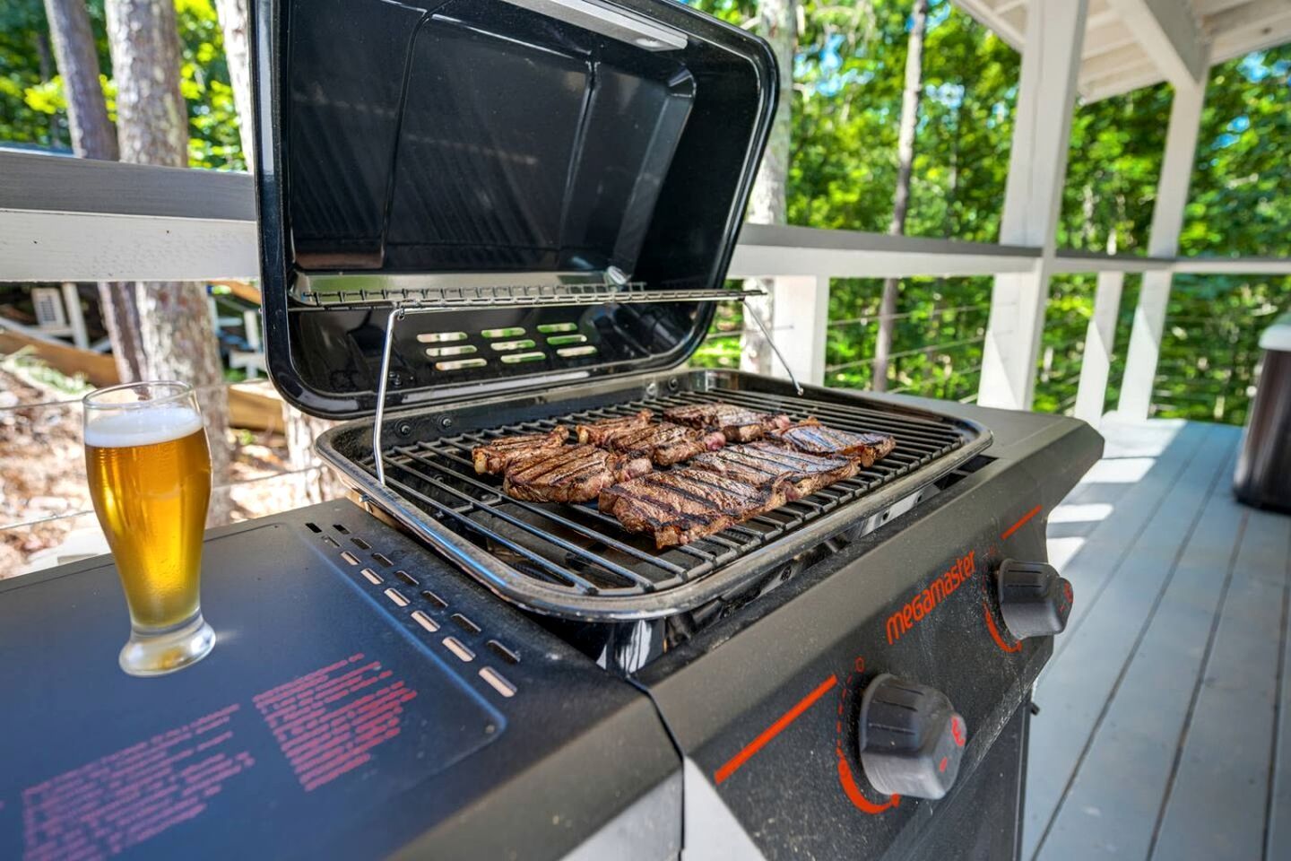 Una parrilla con filetes a la parrilla, una cerveza en un vaso y un área exterior techada.