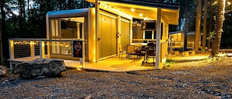 Una cabaña moderna y luminosa con terraza, televisor y un letrero que anuncia una atracción cercana.