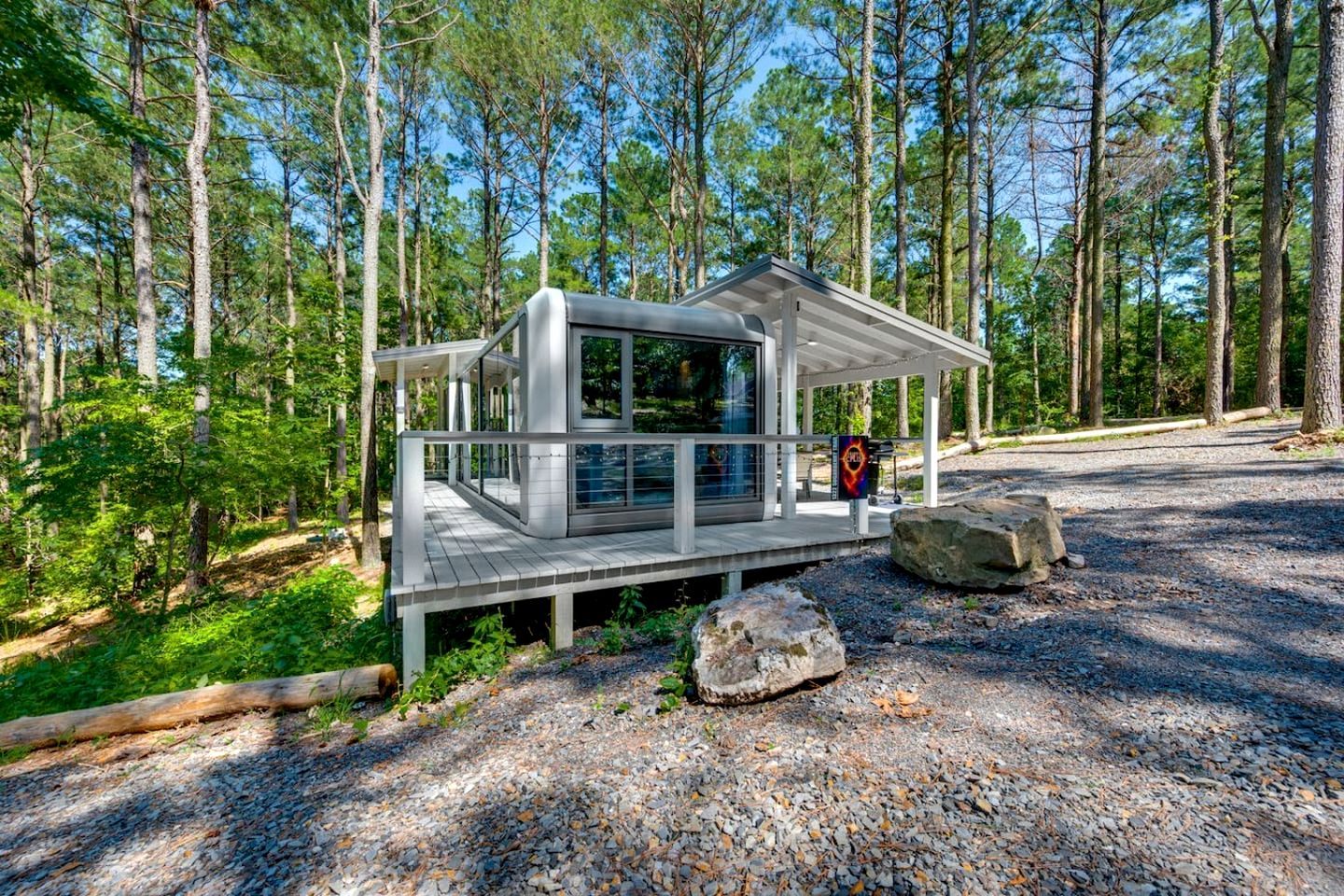 A modern cabin with a deck, surrounded by a forest.