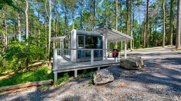 A modern cabin with a deck, surrounded by a forest.