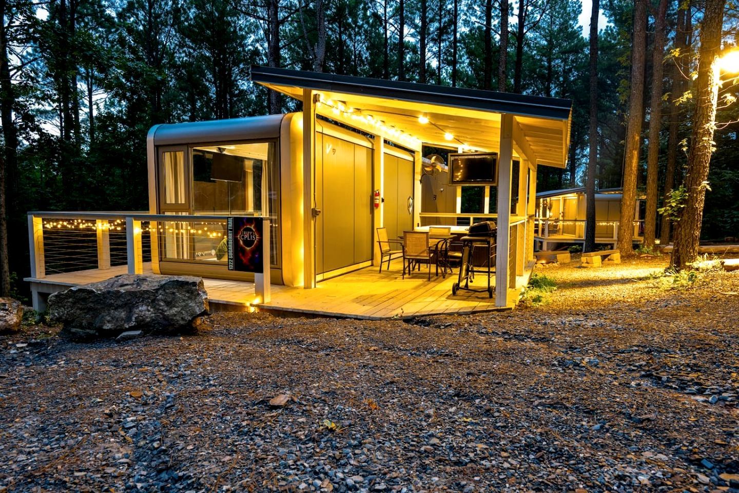 Una cabaña moderna y luminosa con terraza, televisor y un letrero que anuncia una atracción cercana.