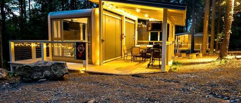 Una cabaña moderna y luminosa con terraza, televisor y un letrero que anuncia una atracción cercana.