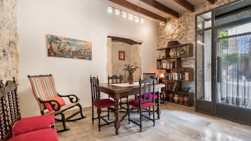 A dining area with a wooden table, chairs, a bookshelf, and a stone wall.