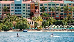 A beachfront hotel with colorful buildings, a pool area with umbrellas, and palm trees. - St. Thomas 2BR Oceanside Villa at Marriott’s Frenchman’s Cove – Beach & Resort A (Southside)
