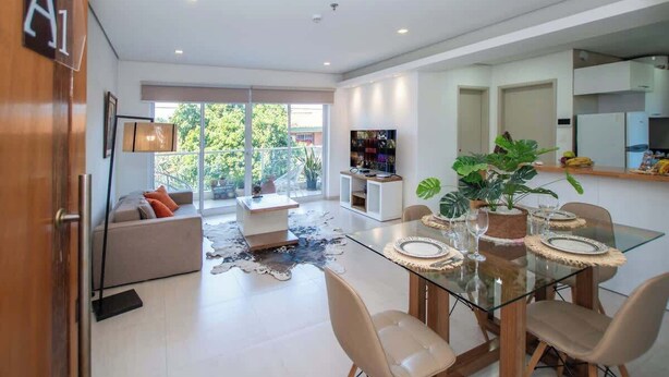A modern living room with a glass dining table, sofa, and TV. - Corporate Stays Edificio Pilar - N2A1 (Asunción)