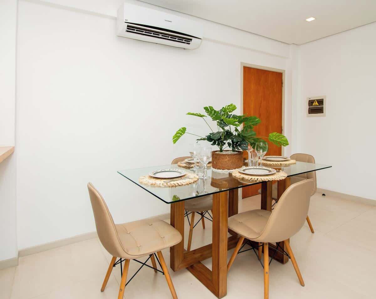 A dining area with a glass table, beige chairs, a potted plant, and a wooden door.