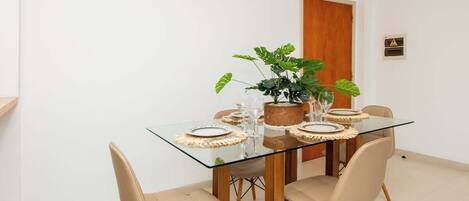 A dining area with a glass table, beige chairs, a potted plant, and a wooden door.