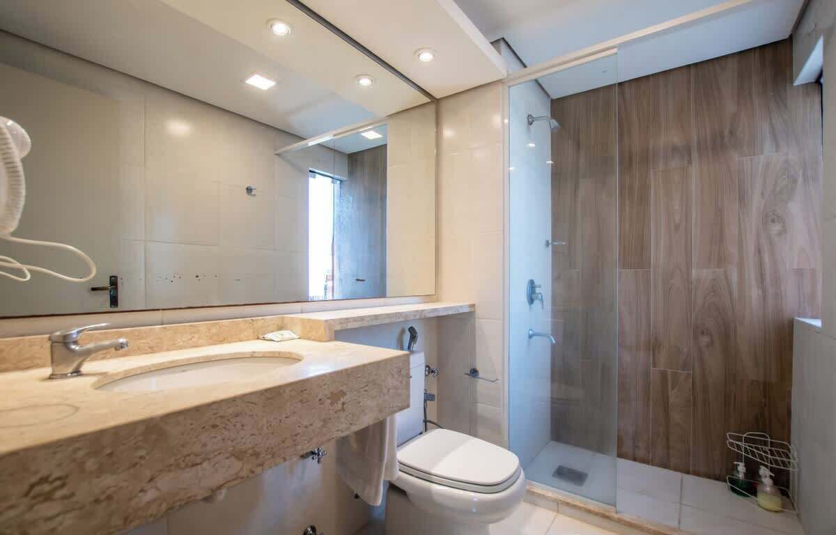 A modern bathroom with a large mirror, a sink, a toilet, and a glass-enclosed shower.