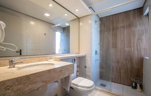 Un bany modern amb un mirall gran, un lavabo, un vàter i una dutxa amb portes de vidre.