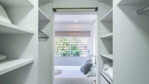 A walk-in closet with open shelving, a bed with pillows, and a view of greenery outside. - Corporate Stays Edificio Pilar - N2A1 (Asunción)