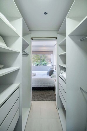 A walk-in closet with open shelving, a bed with pillows, and a view of greenery outside. - Corporate Stays Edificio Pilar - N2A1 (Asunción)
