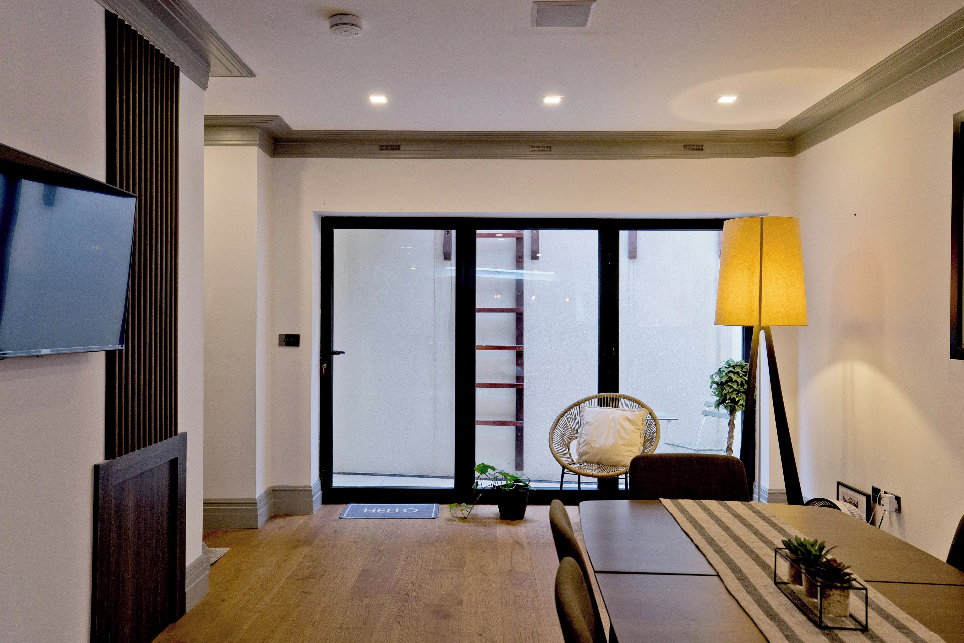 Un comedor moderno con una mesa de madera, sillas, un televisor en la pared y un gran ventanal con vistas al exterior.