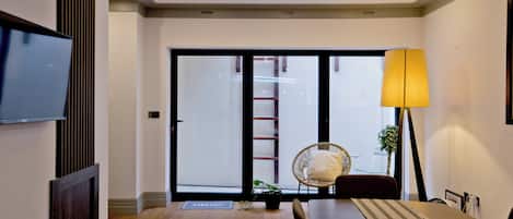 Un comedor moderno con una mesa de madera, sillas, un televisor en la pared y un gran ventanal con vistas al exterior.
